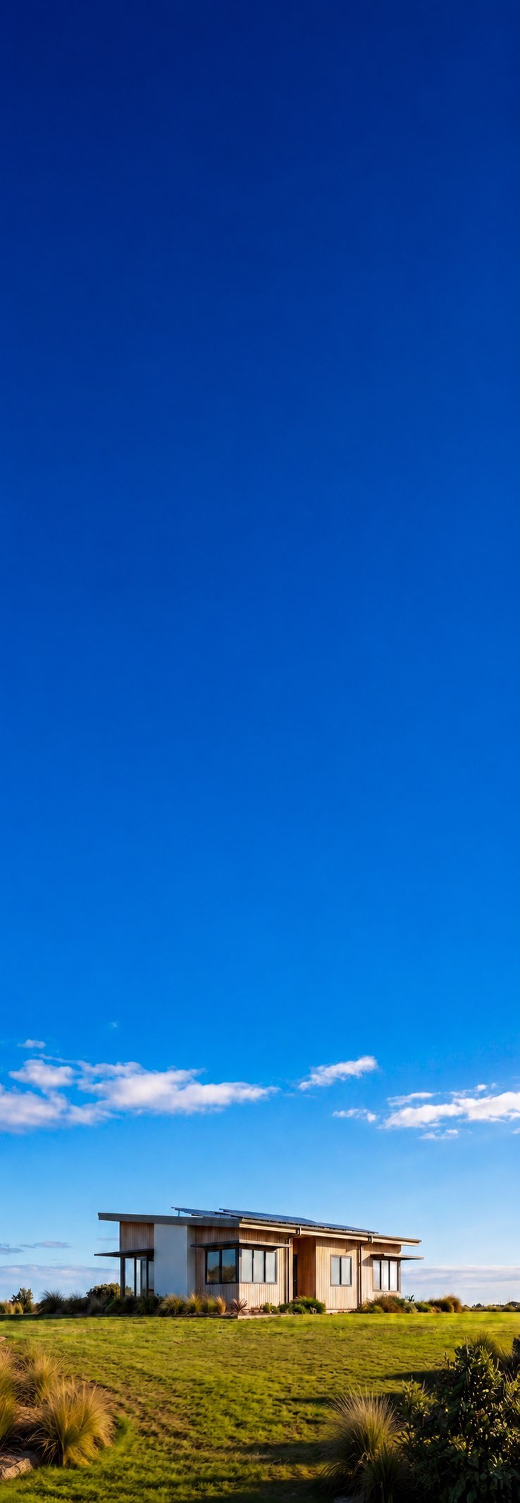 Modern single-story Passive House with solar panels under open blue sky, portrait view